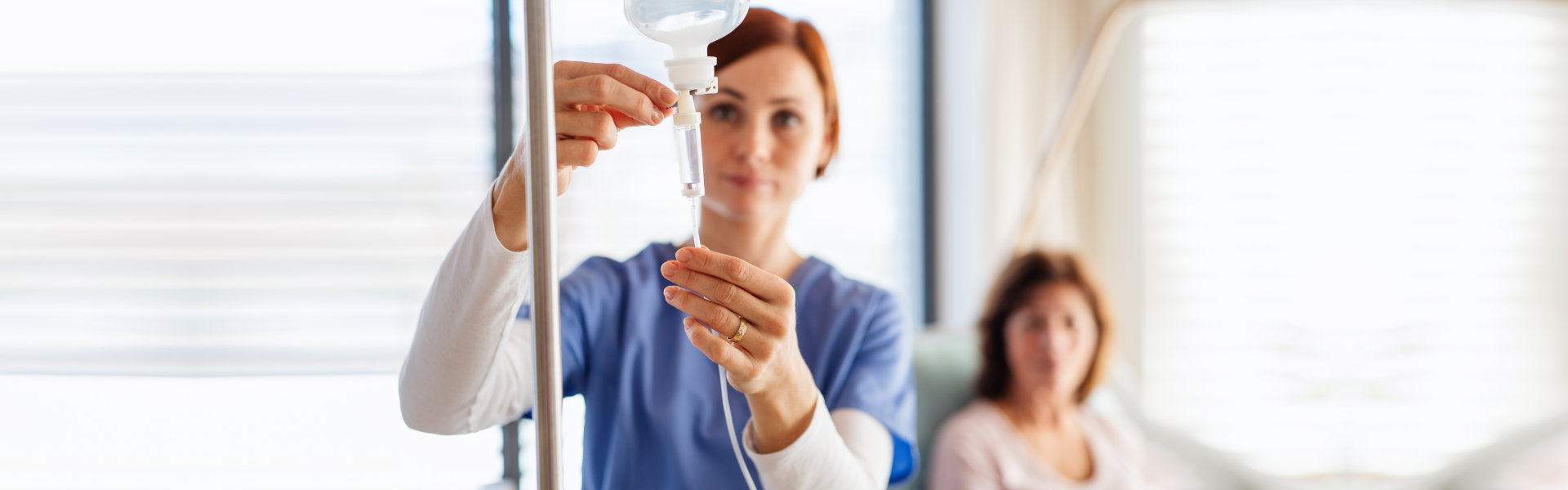 A nurse with IV drip and patient in bed in hospital room.